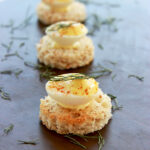 three deviled quail eggs placed over toasted bread cut into rounds.