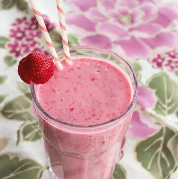 Red Berry Smoothie in a large glass topped with a strawberry and two white and pink straws.