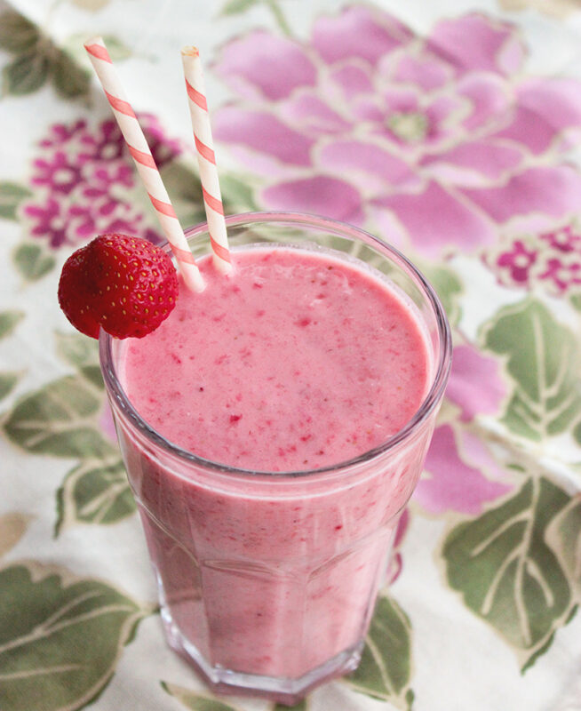 Red Berry Smoothie in a large glass topped with a strawberry and two white and pink straws.