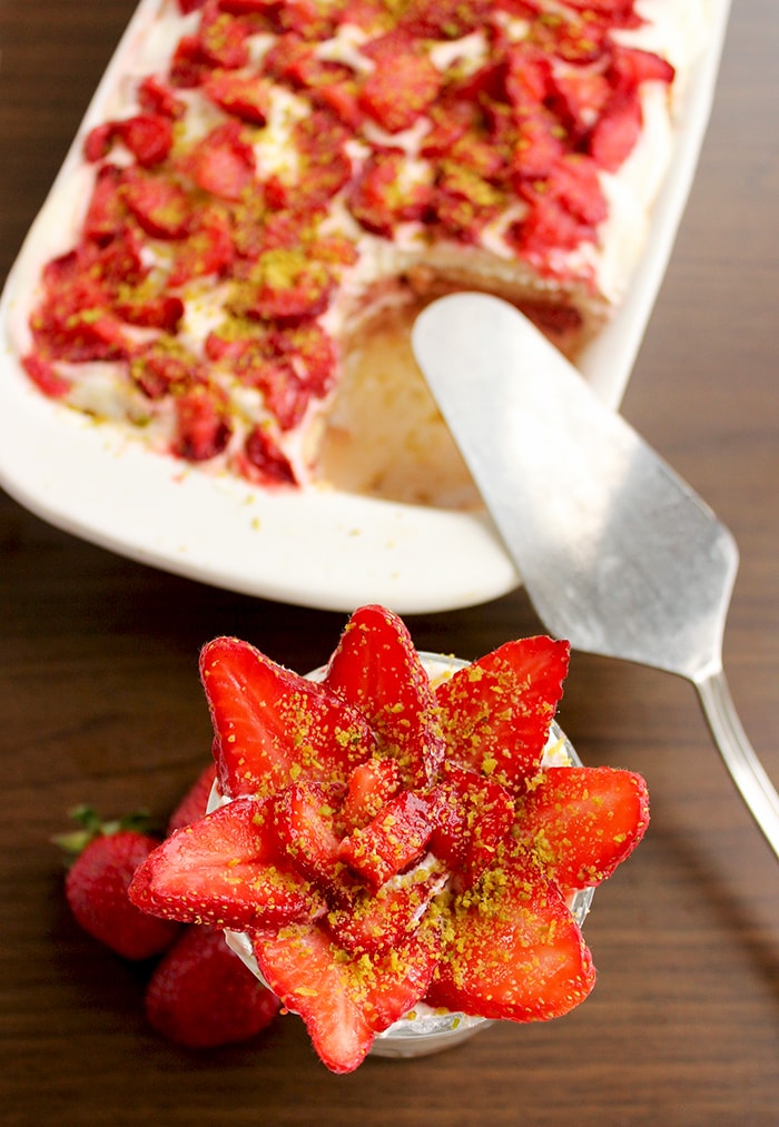 Strawberry Tiramisu served in a glass, a large baking dish with strawberry tiramisu in the background next to a cake cutter.
