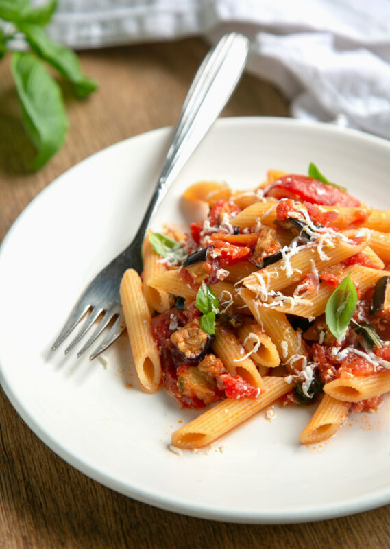 penne pasta alla norme topped with basil leaves on a plate next to a fork