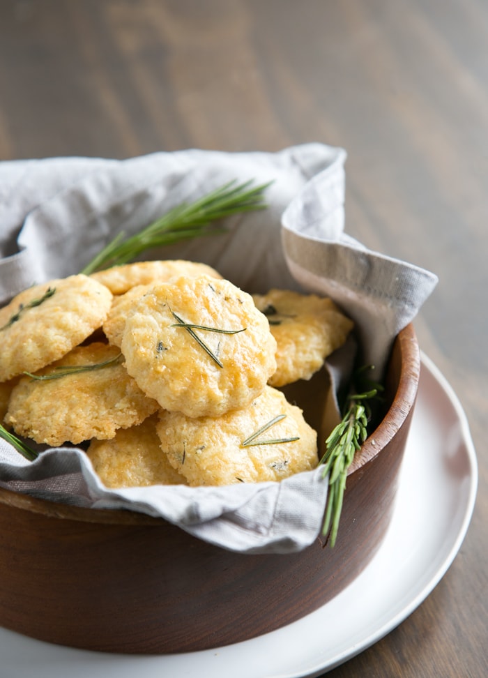 Parmesan cookies in a large wooden bowl covered with grey napkin, white plate beneath and wood table in the background.