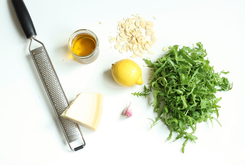 recipe ingredients: parmesan cheese and a grater, lemon, extra virgin olive oil, almond flakes, garlic and rocket leaves