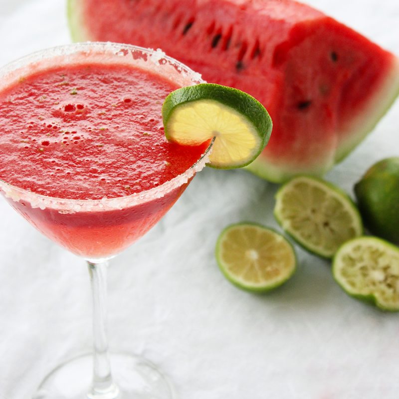 watermelon margarita served in a martini glass and decorated with a lime slice.