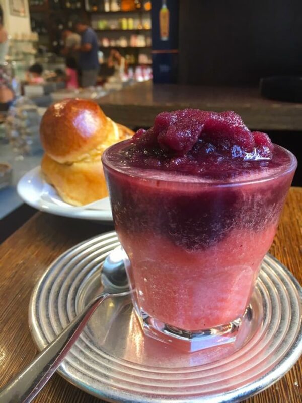 blackberry and strawberry granita in a glass over a silver plate with a teaspoon, sicilian brioche in the background