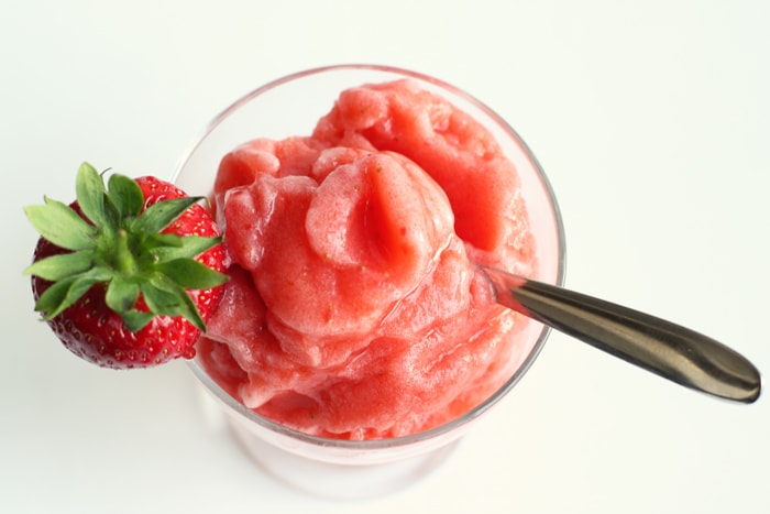 Strawberry Sicilian granita in a glass topped with a fresh strawberry and spoon