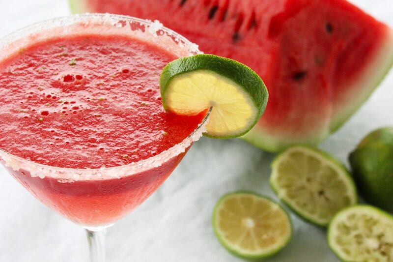 Watermelon margarita served in amartini glass and decorated with a lime slice.