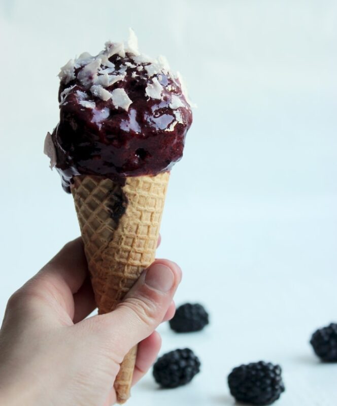 hand holding a cone with 2-ingredient blackberry ice cream topped with coconut flakes