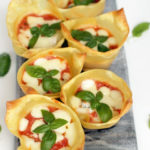italian lasagna cups on a grey board, basil leaves scattered over the white background