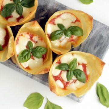 flat lay image of italian lasagna cups on grey board, basil leaves scattered over the white background