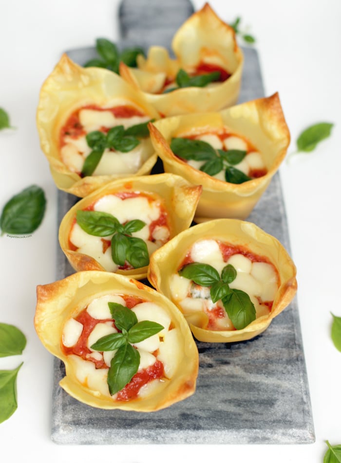 italian lasagna cups on a grey board, basil leaves scattered over the white background