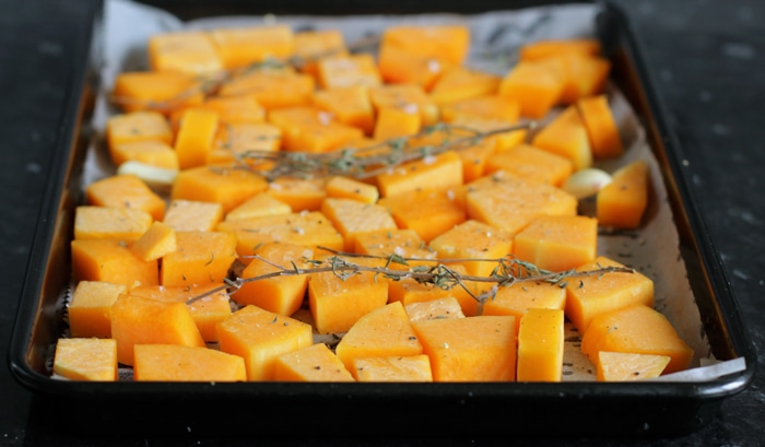 pumpkin cubes topped with thyme sprigs in a baking tray covered with parchment paper.