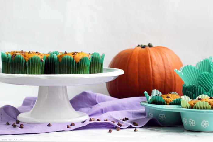 dairy-free pumpkin muffins on a cake stand and on a muffin tin, pumpkin in the background