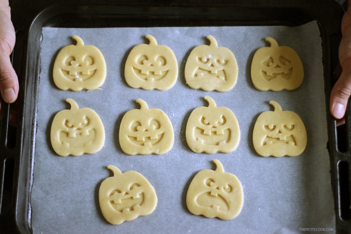 pumpkin shaped halloween italian shortbread cookies raw on baking tray covered with parchment paper held by two hands