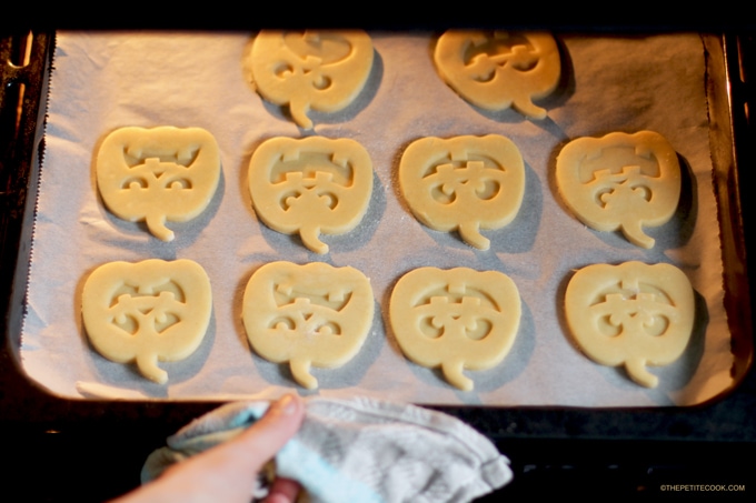 Hand putting the pumpkin shaped italian shortbread cookies on baking tray with parchment paper in the oven