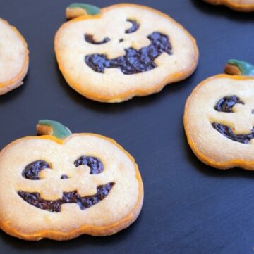Pumpkin-shaped Halloween Italian Shortbread Cookies recipe on black background next to half pumpkin