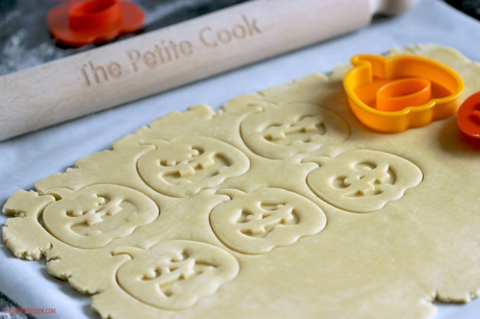  Italian Shortbread Cookies dough rolled and cookies cut into pumpkin shapes, next to The Petite Cook rolling pin and orange pumpkin cookie cutters