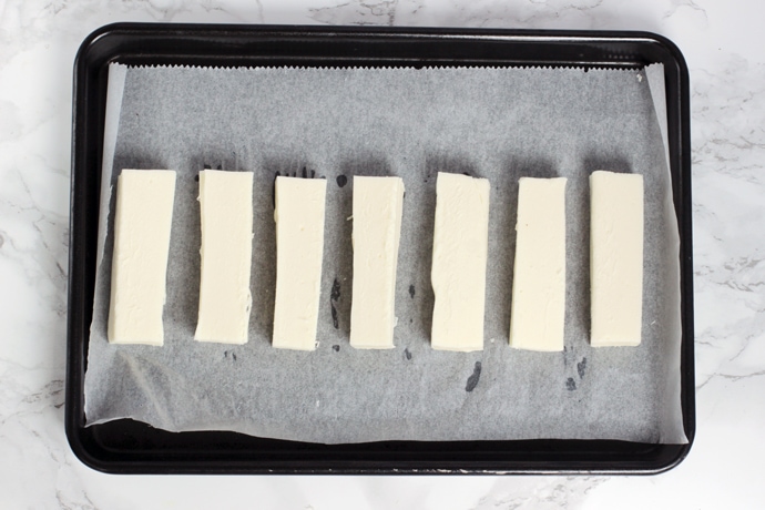 recipe process step 1: mozzarella sticks on a baking tray covered with kitchen paper