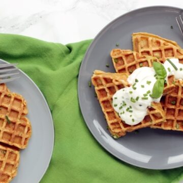 sweet potato waffles topped with sour cream and chives served onto two plates.