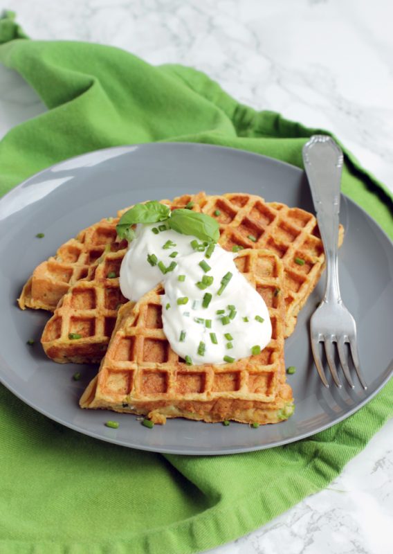 Three sweet potato waffles topped with sour cream and chives, served on a plate.