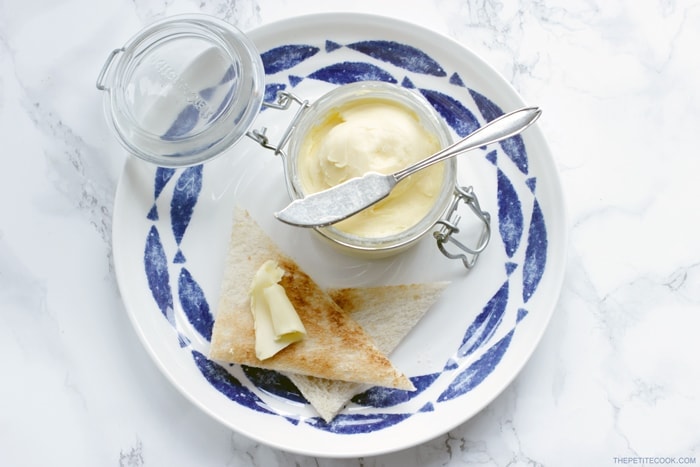 homemade butter in a jar with a knife over it, bread toasted with butter on top on a large plate