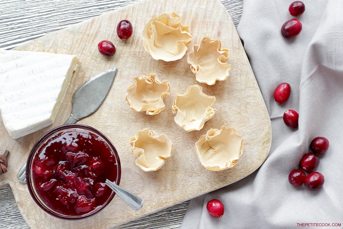 phyllo cups on a wood board next to homemade cranberry sauce and brie cheese