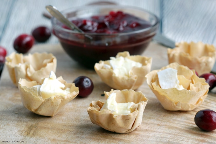 recipe step 2: phyllo cups filled with brie cheese, homemade cranberry sauce in the background
