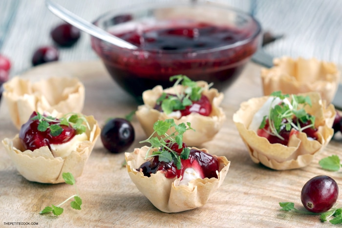 brie and cranberry cups on a wood board, homemade cranberry sauce in the background