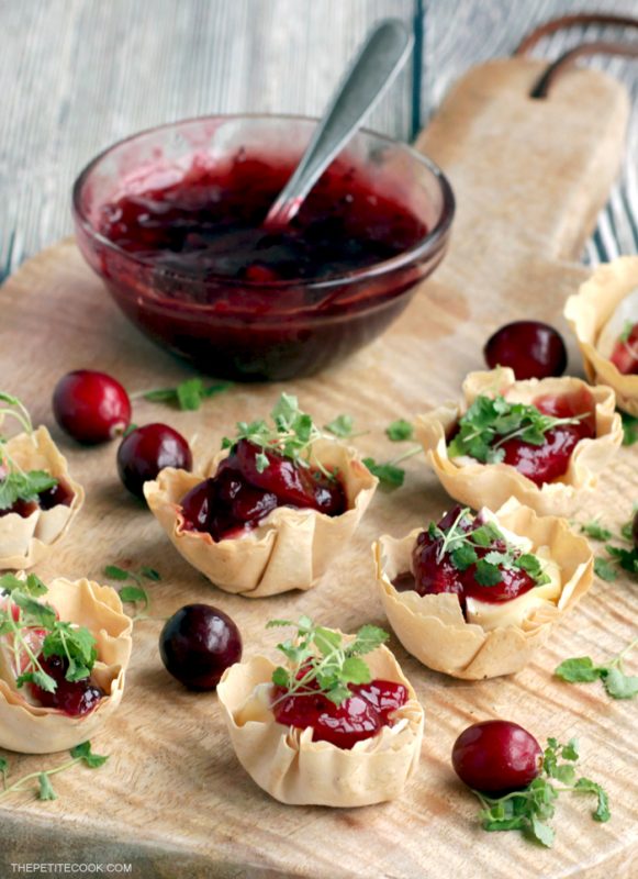 brie and cranberry cups on a wood board, homemade cranberry sauce in the background