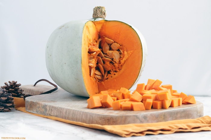 open pumpkin and cubes on wood board over orange napkin with two pine cones in the background
