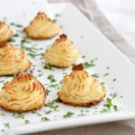 Easy duchess potatoes decorated with parsley on a white serving dish