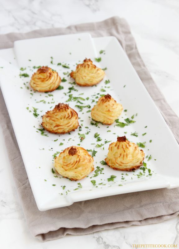 Easy duchess potatoes decorated with parsley on a large white serving dish over a beige napkin