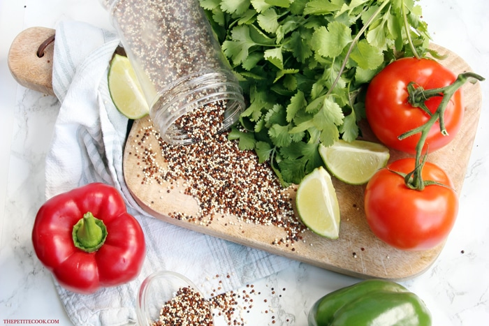 mixed quinoa, cilantro, lime wedges, tomatoes and bell peppers on a wood board