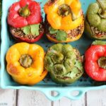 6 quinoa stuffed bell peppers in a large baking dish, next to lime wedges and bunch of cilantro
