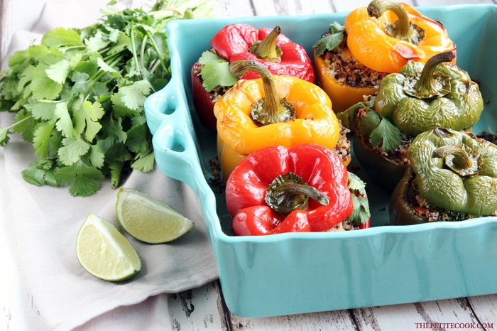  Quinoa Stuffed Bell Peppers in a baking dish, next to lime wedges and cilantro on the side