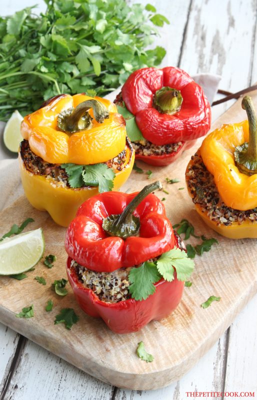 red and yellow quinoa stuffed bell peppers on a wood board, served with lime wedges and cilantro on the side.