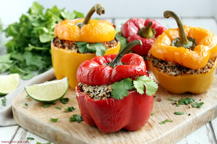three quinoa stuffed bell peppers served on a wood board with lime wedges.