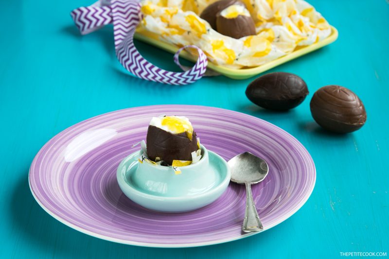 Cheesecake Chocolate Eggs on egg holder over a purple plate next to a spoon, more cheesecake eggs in the background