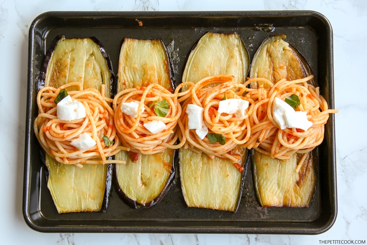 Eggplant spaghetti sandwiches process: baking tray with eggplant slices and spaghetti nests on top and cubed mozzarella
