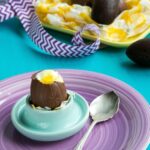 Cheesecake Chocolate Eggs on egg holder over a purple plate next to a spoon, more cheesecake eggs in the background