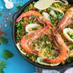 healthy seafood paella topped with grilled shrimps, calamari and lemon wedges