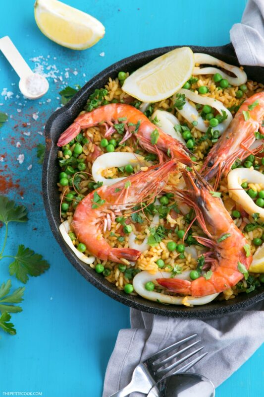 Paella topped with grilled shrimps, calamari and lemon wedges