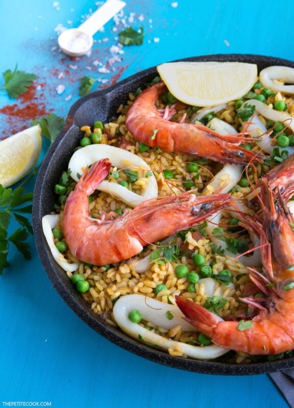 Paella topped with grilled shrimps, calamari and lemon wedges