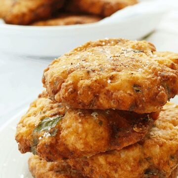 cauliflower fritters stacked on a white plate, more fritters in a plate on the background