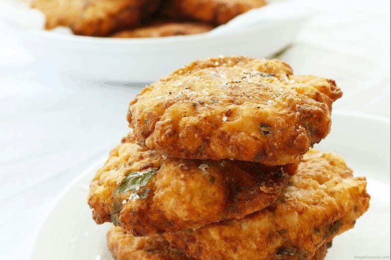 cauliflower fritters stacked on a white plate, more fritters in a plate on the background