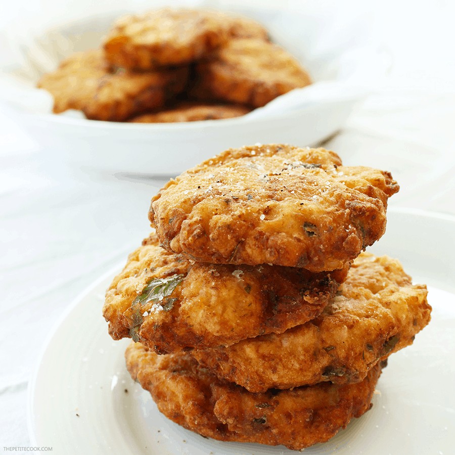 cauliflower fritters stacked on a white plate, more fritters in a plate on the background