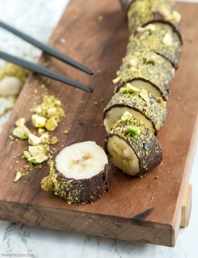 Pistachio Chocolate Banana Sushi on a wood board, with chopsticks on the side.