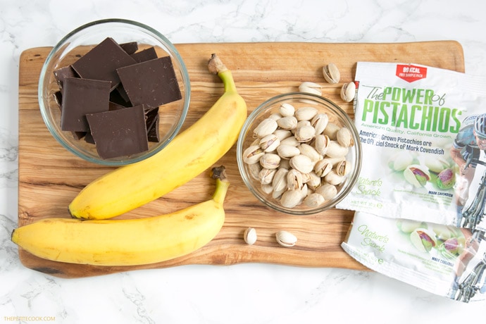 recipe ingredients: chopped dark chocolate, banana, pistachios on a wood board.