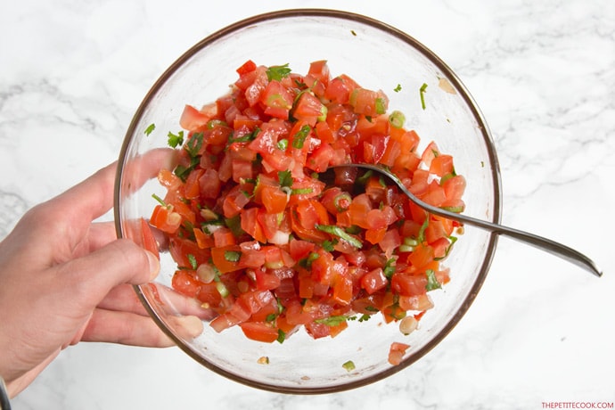 hand holding zucchini boats pico de gallo filling in a large clear glass bowl