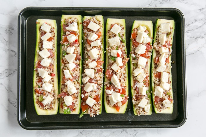 zucchini boats stuffed with quinoa and pico de gallo, and topped with mozzarella cheese, arranged on a baking tray